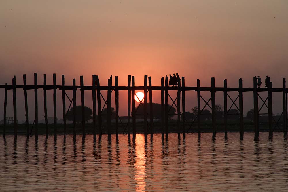 Sunset reflecting in water over a tall wooden bridge with silhouettes of three people