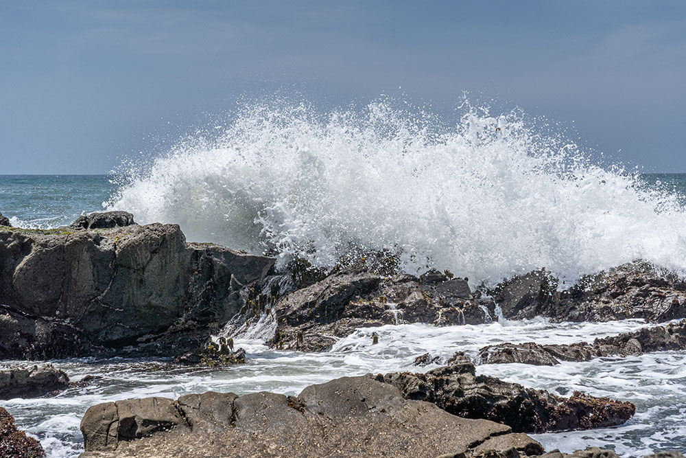 Close-up of an ocean wave crashing into rocks under a clear blue sky