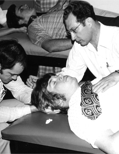 Man lays on a table as two men hold his head and his chest